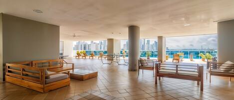 A spacious indoor area with wooden benches and a view of a city skyline through large windows.