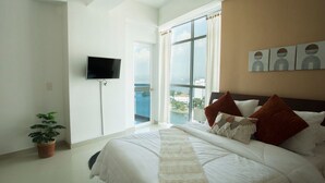 A bedroom with a large bed, a TV mounted on the wall, a potted plant, and a balcony with a view of the city. - Poseidon del Caribe (Cartagena)