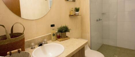 Un bagno con lavandino, toilette e doccia. Sono presenti mensole con articoli da toilette e uno specchio sopra il lavandino.