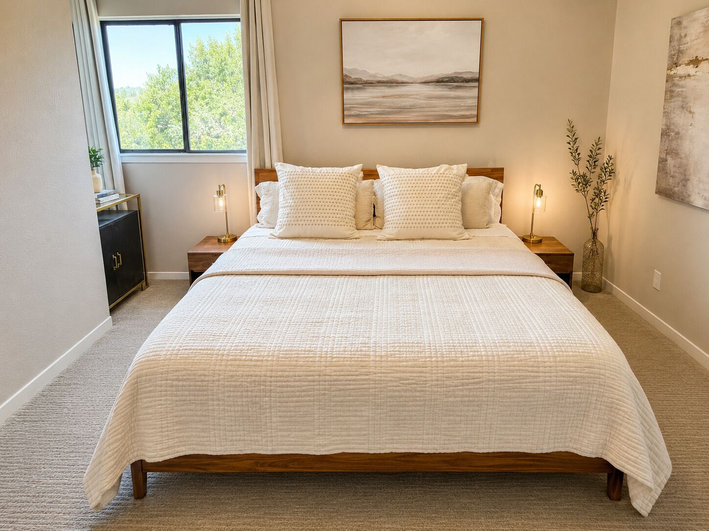 Ein Schlafzimmer mit einem großen Bett, zwei Nachttischen, einem Schminktisch, einem Fenster mit Vorhängen, einem Wandbild und einer Vase mit Pflanzen.