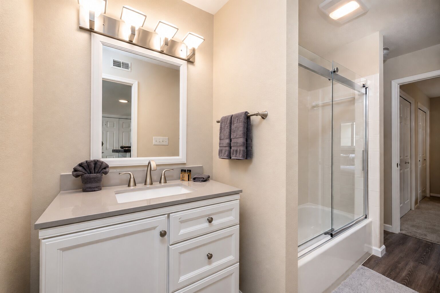 A bathroom with a sink, mirror, vanity, towel rack, and a glass shower enclosure.