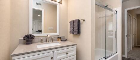 A bathroom with a sink, mirror, vanity, towel rack, and a glass shower enclosure.