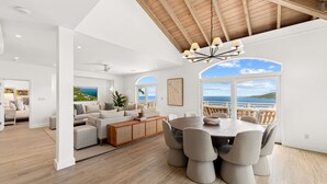 A spacious living area with a wooden ceiling, a dining table with chairs, and a view of the sea through large windows. - Generator! 2 Primary Bedrooms - Magens Bay - Dining (St. Thomas)