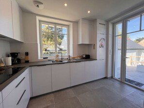 Eine moderne Küche mit großem Fenster, weißen Schränken und einer Arbeitsplatte mit verschiedenen Geräten.