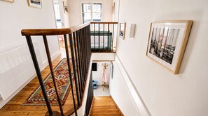 Eine Treppe mit hölzernem Geländer führt zu einer Empflage mit einem gemusterten Teppich und einem gerahmten Bild an der Wand.