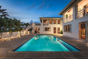 Une maison à deux étages avec une piscine, un espace salon extérieur et un balcon.