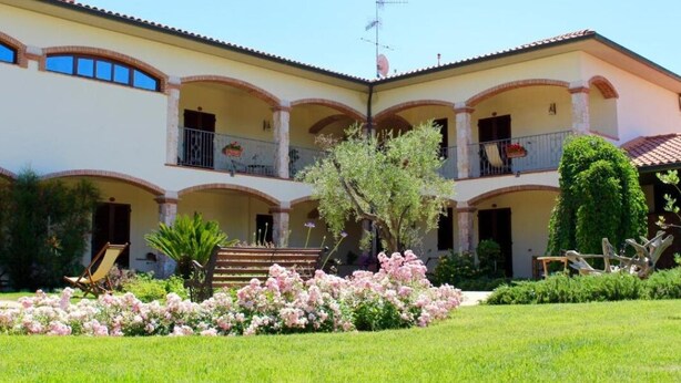 Un edificio de dos pisos con un patio central, balcones y un jardín bien cuidado con flores rosadas.