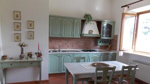 Una cocina con gabinetes verdes, salpicadero de azulejos, una ventana con cortina y una mesa de comedor con sillas.