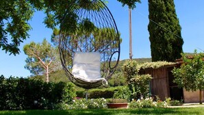 Un sillón hamaca en un jardín exuberante con una estructura de madera al fondo.