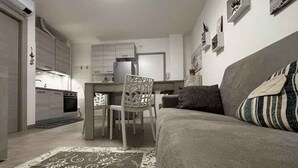 Un salon moderne avec un canapé gris, un tapis à motifs et un coin repas comprenant une chaise et une table blanches.
