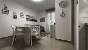 Un coin repas avec une table ronde et des chaises, un canapé et un petit espace cuisine équipé d’un réfrigérateur et d’une horloge murale.