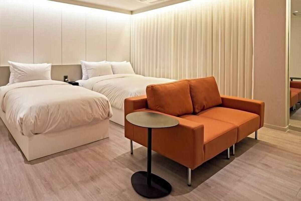 Una habitación de hotel moderna con dos camas, un sofá y una pequeña mesa redonda.