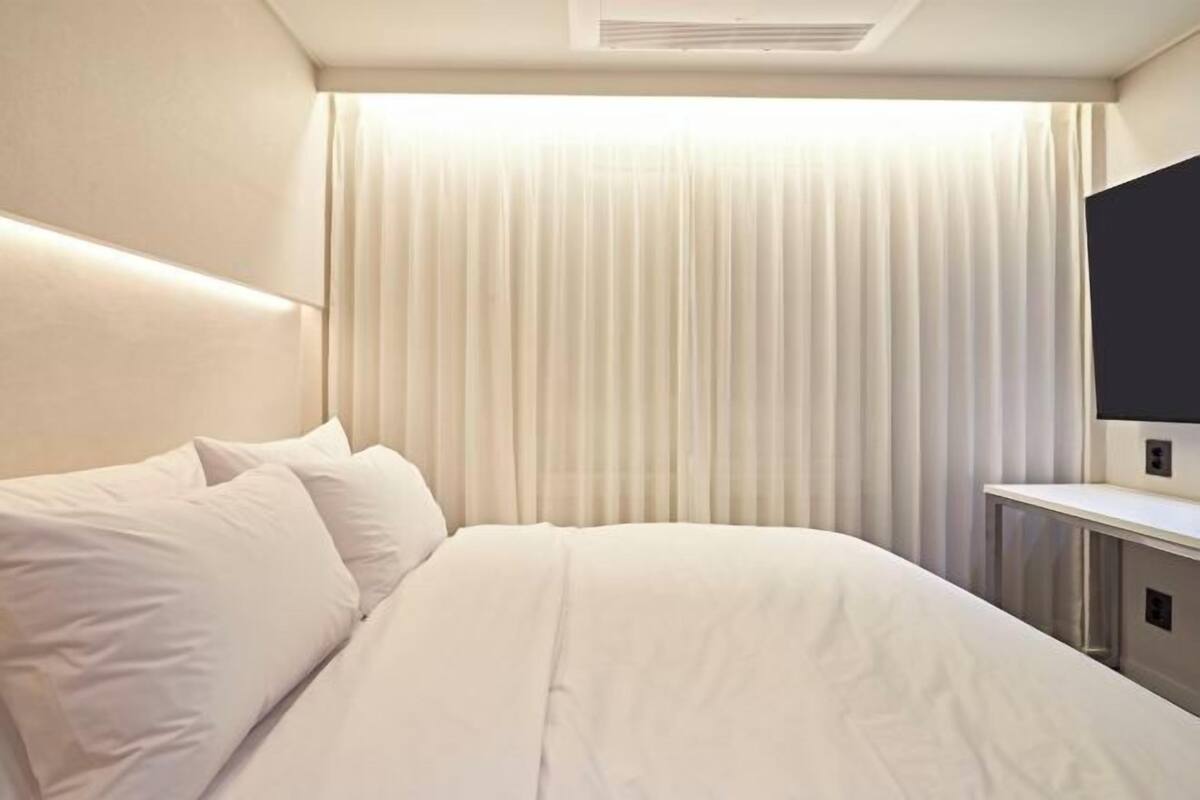 Una habitación de hotel con una cama, un televisor de pantalla plana y un ventanal con cortinas.