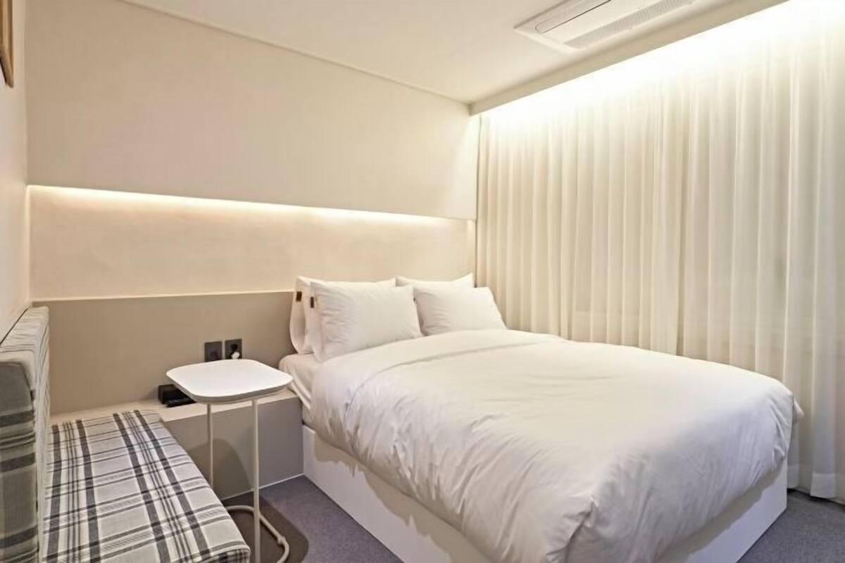 Una habitación de hotel con cama, mesita de noche y un banco.