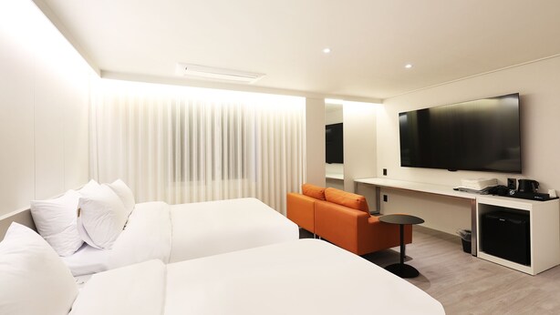 Habitació d'hotel moderna amb un llit gran, un sofà, una taula petita, un televisor i una nevera minibar.