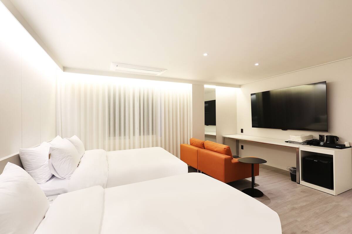 Habitación de hotel moderna con una cama grande, un sofá, una mesita, un televisor y un minibar.