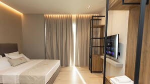 Une chambre d’hôtel moderne équipée d’un lit, d’une télévision, d’une armoire en bois et d’une grande fenêtre avec des rideaux.