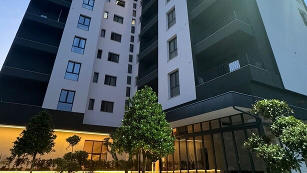 Un bâtiment moderne à plusieurs étages, doté d’une façade aux couleurs contrastées, de grandes fenêtres et d’un hall d’entrée bien éclairé agrémenté de plantes en pot.