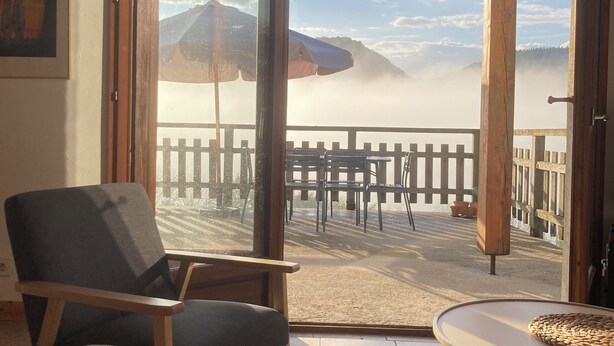 Ein Zimmer mit Blick auf einen nebelverhangenen Berg, Holzmöbel und ein großes Fenster.