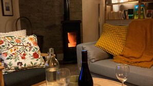 Ein gemütliches Wohnzimmer mit einem runden Holztisch, einer Couch mit floralen Kissen, einem Bücherregal und einem Kamin.