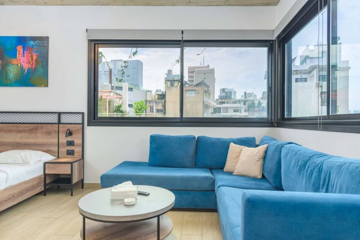 Una sala de estar moderna con un sofá azul, una mesa de centro redonda y una cama con cabecera de madera.