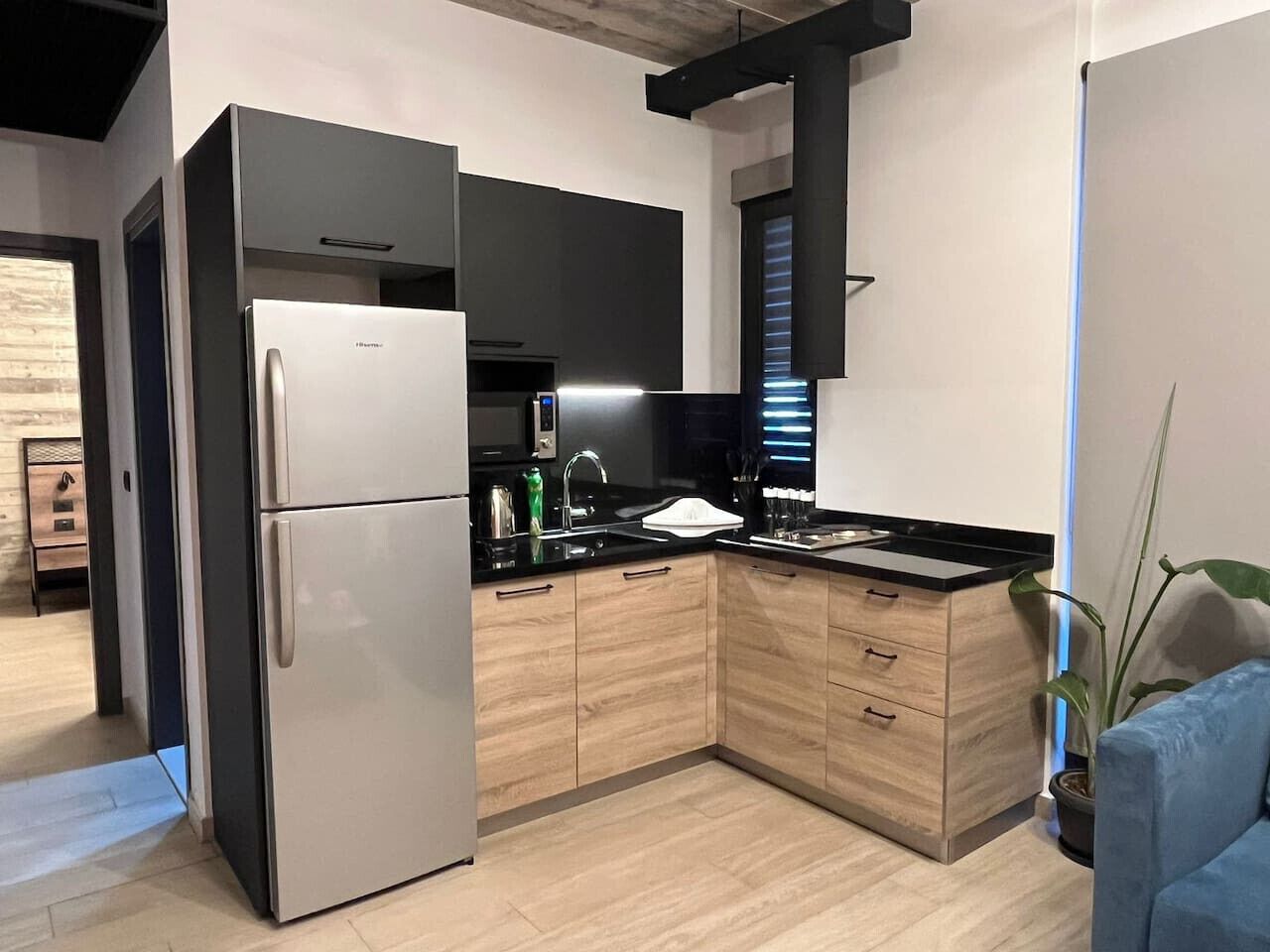 Eine moderne Küche mit einem eingebauten Kühlschrank, Holzschränken, einer schwarzen Arbeitsplatte und einem Fenster mit Jalousien.