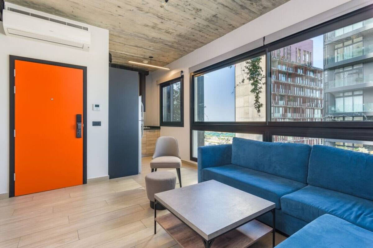 Un interior moderno con un sofá azul, una mesita y una puerta naranja.