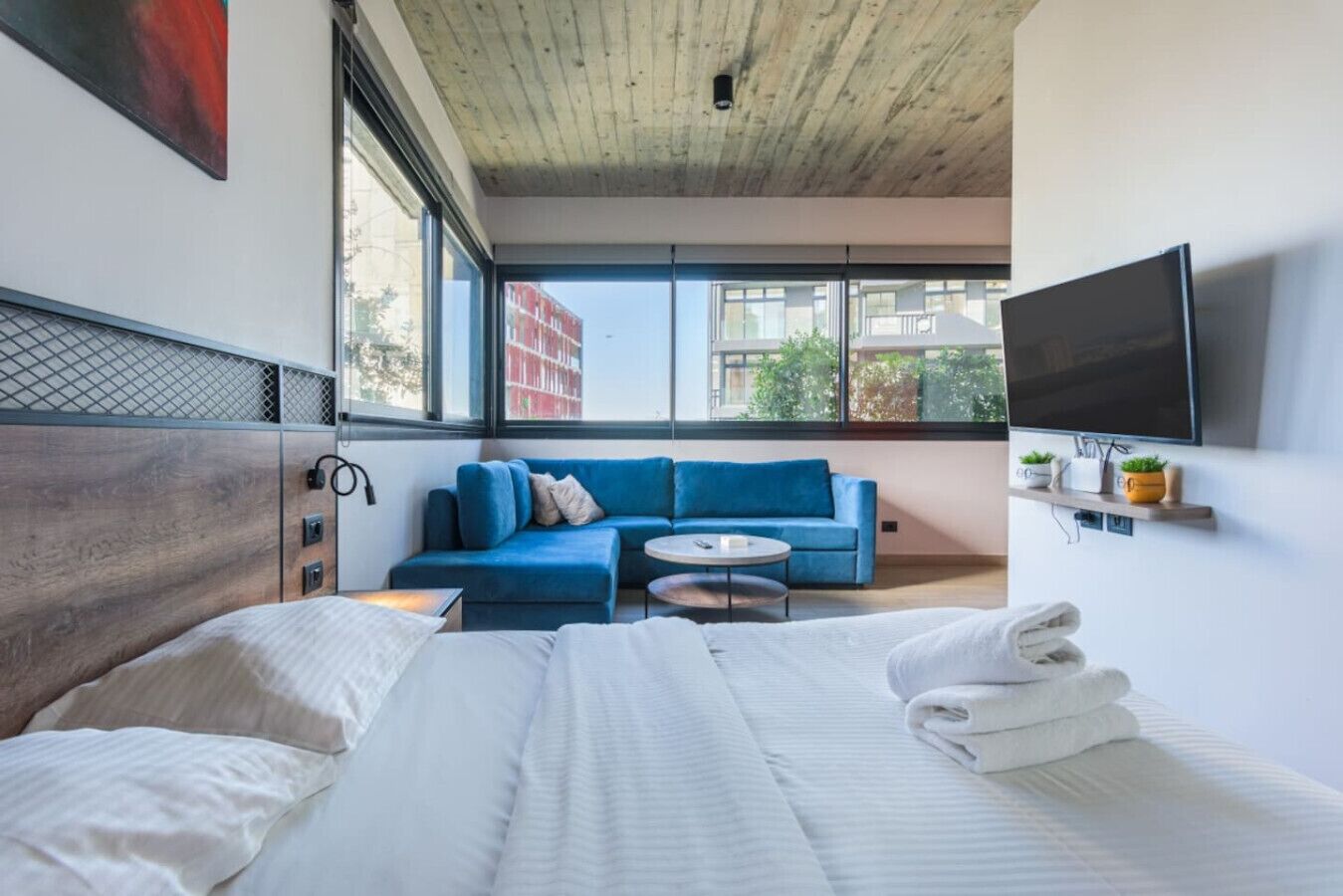 Een moderne hotelkamer met een groot bed, een blauwe bank, een klein rond tafeltje en een aan de muur bevestigde televisie.