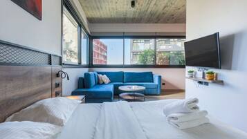 Een moderne hotelkamer met een groot bed, een blauwe bank, een klein rond tafeltje en een aan de muur bevestigde televisie.