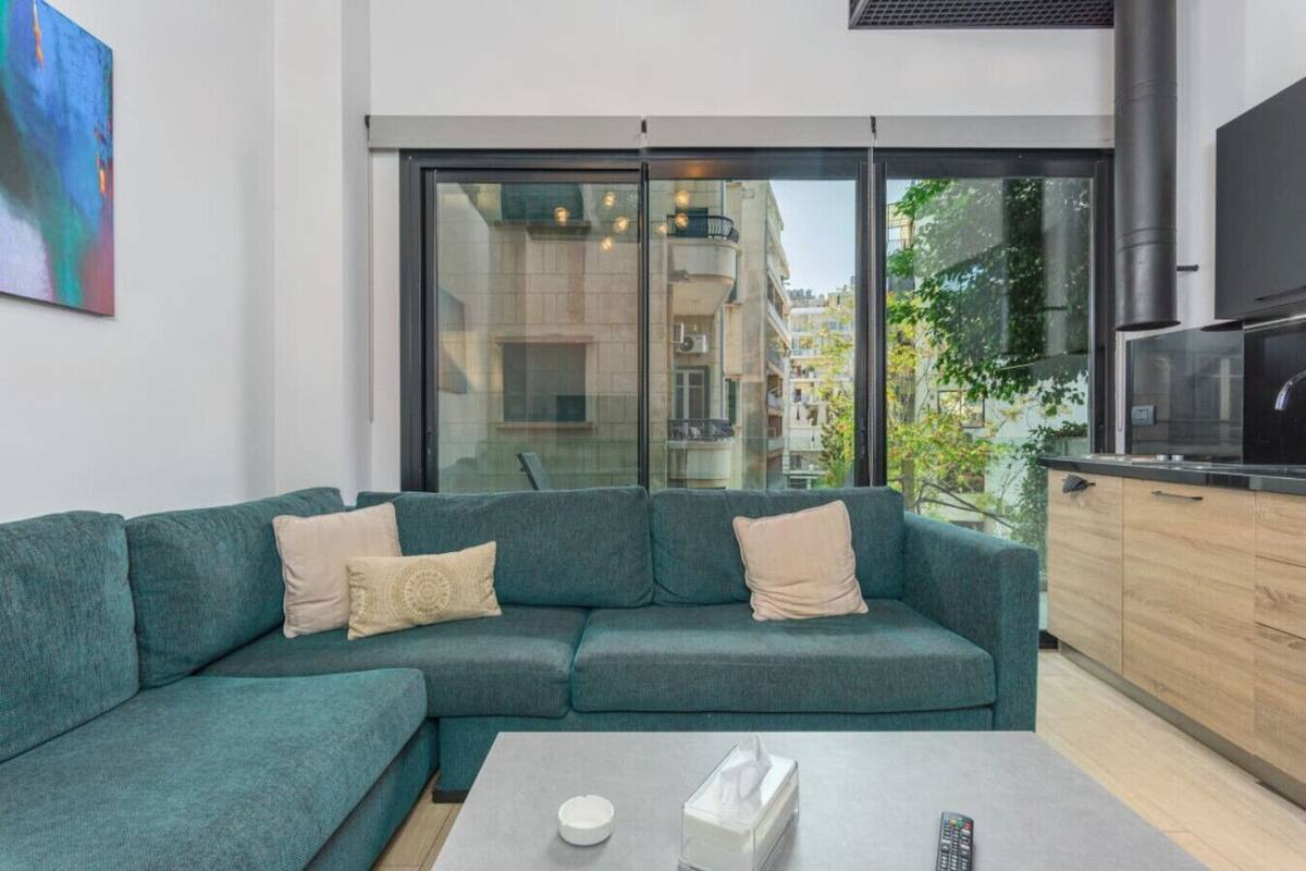 Una sala de estar moderna con un sofá color turquesa, una mesa de centro y una cocina con televisor y armarios.