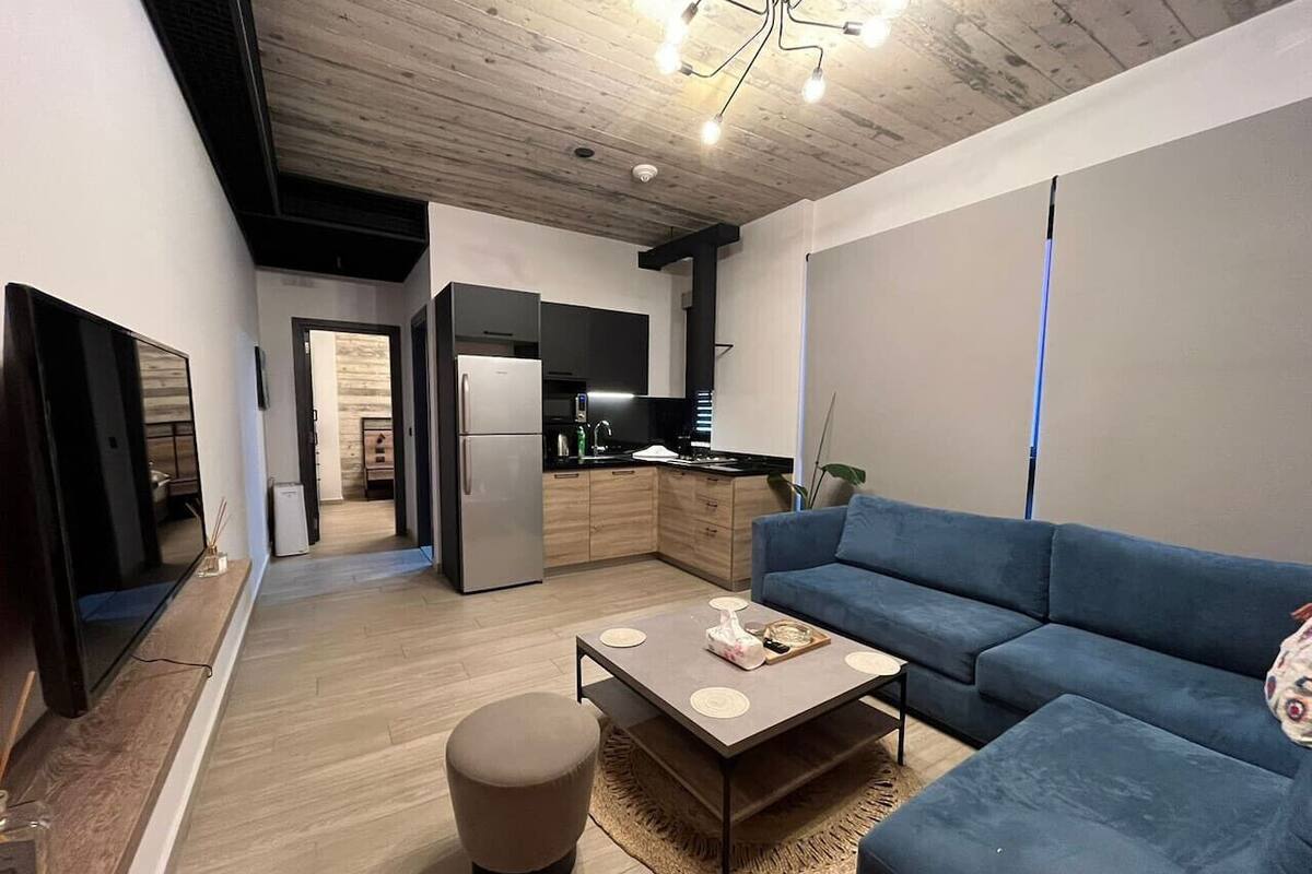 Un salón moderno con un sofá azul, una mesa de centro y una cocina al fondo.