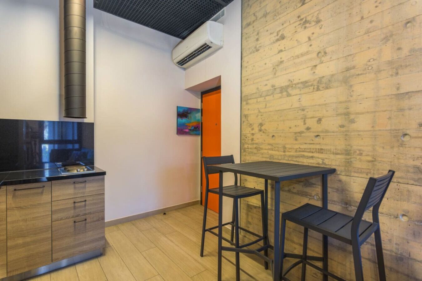 A compact kitchen with a modern stove, a wooden wall, and a small dining area with two chairs and a table.