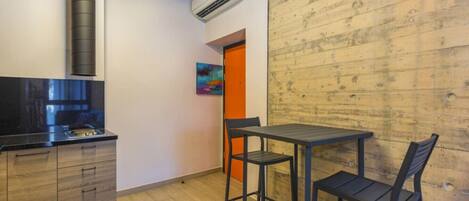 A compact kitchen with a modern stove, a wooden wall, and a small dining area with two chairs and a table.