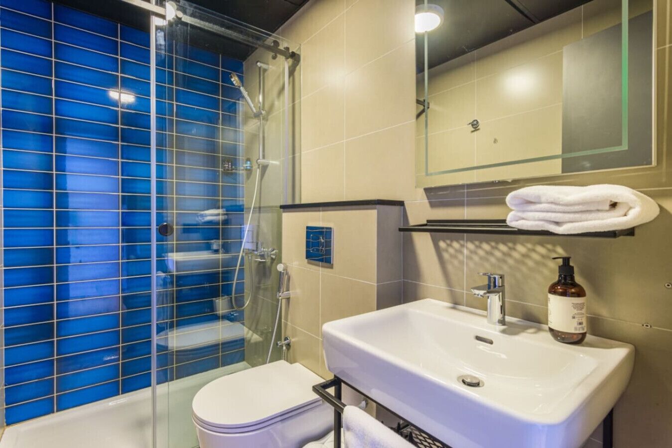 A modern bathroom with a glass-enclosed shower, a white sink, and a beige tiled wall.