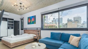 A modern room with a bed, a blue sofa, a round coffee table, and a city view through large windows. - Amine Apart-Hotel by Stayinn (Beirut)