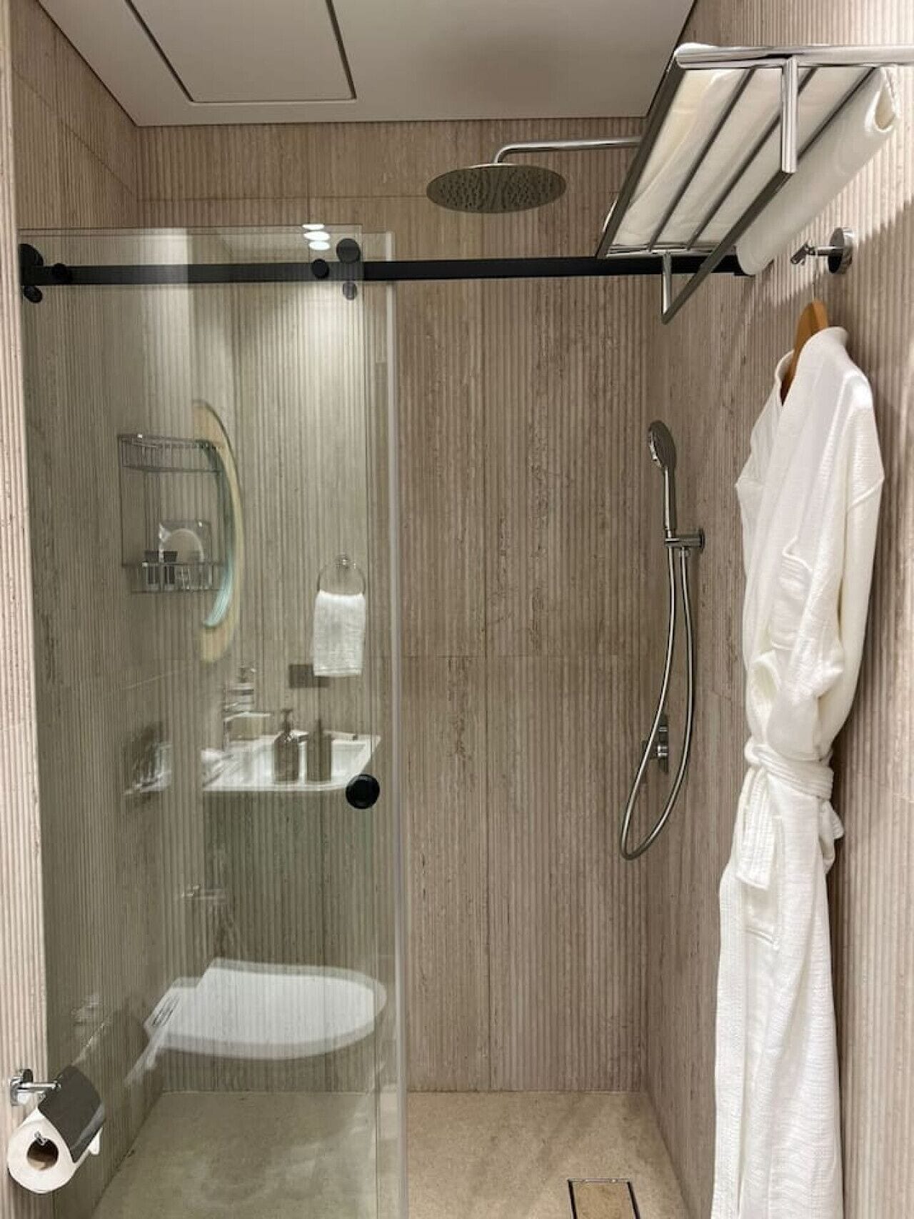 A modern bathroom with a glass-enclosed shower, a towel rack, and a white robe hanging on the wall.
