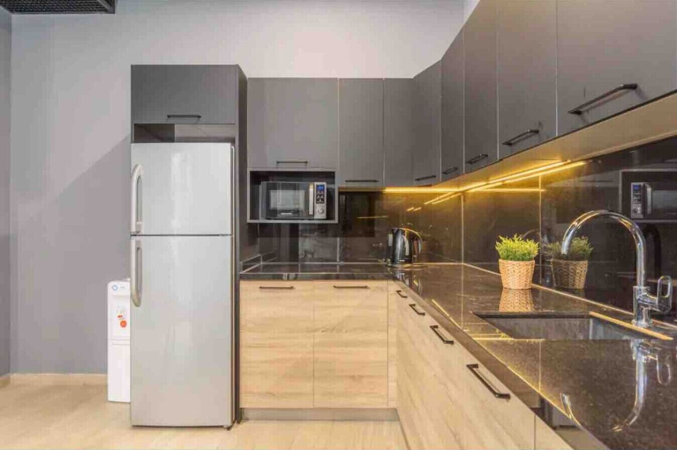A modern kitchen with a refrigerator, microwave, and stainless steel sink.