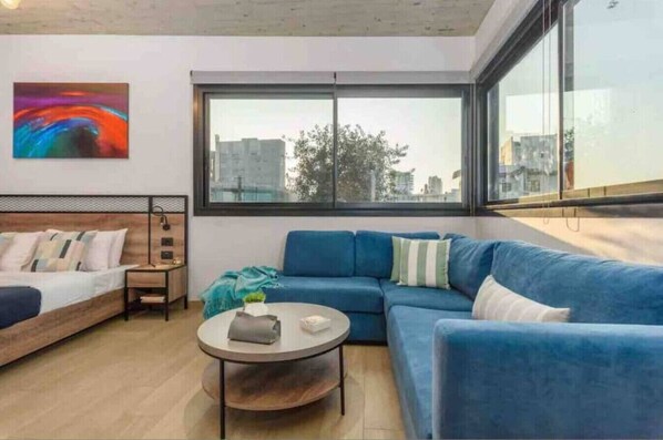 A modern living room with a blue sofa, a round coffee table, and a bed with a wooden headboard. - Amine Apart-Hotel by Stayinn (Beirut)