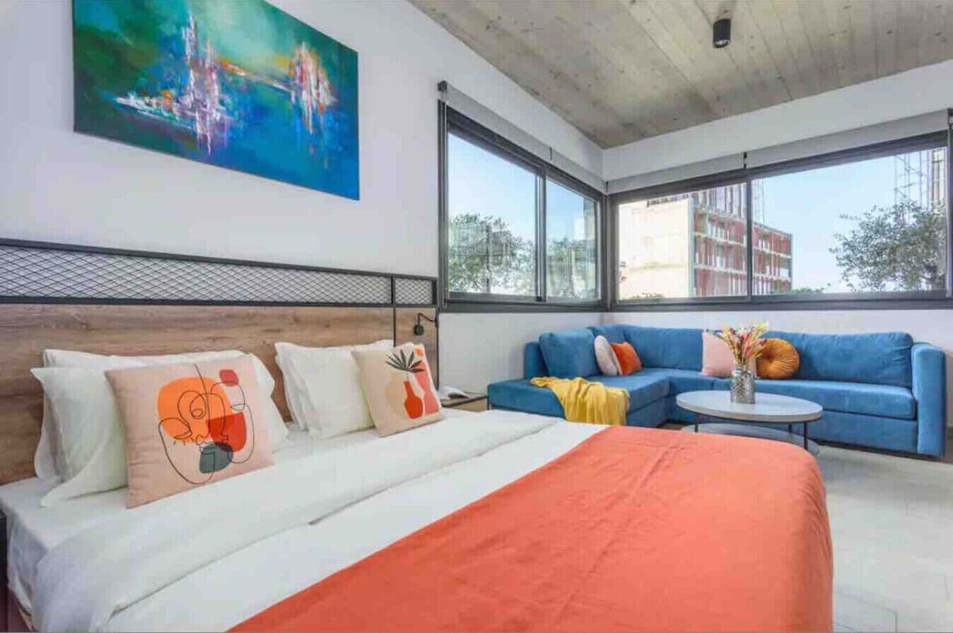 A modern hotel room with a large bed, a blue sofa, and a round coffee table.
