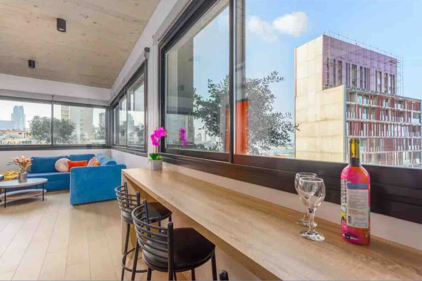 A modern interior with a wooden bar, seating area, and large windows offering a city view.