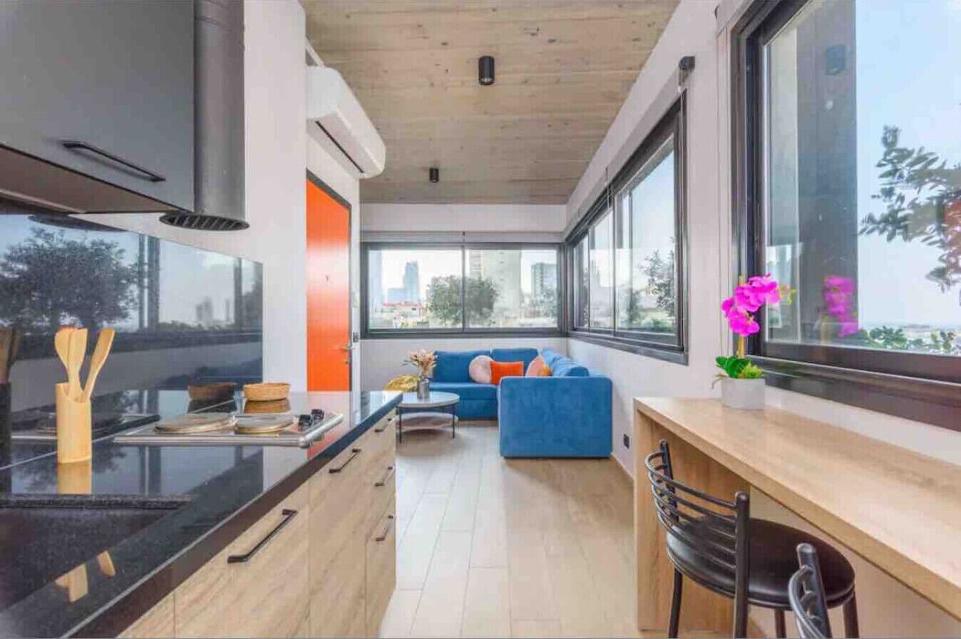 A modern kitchen with a black countertop, wooden cabinets, and a window overlooking a cityscape.