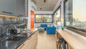 A modern kitchen with a large window, a dining area with a blue sofa, and a city view. - Amine Apart-Hotel by Stayinn (Beirut)