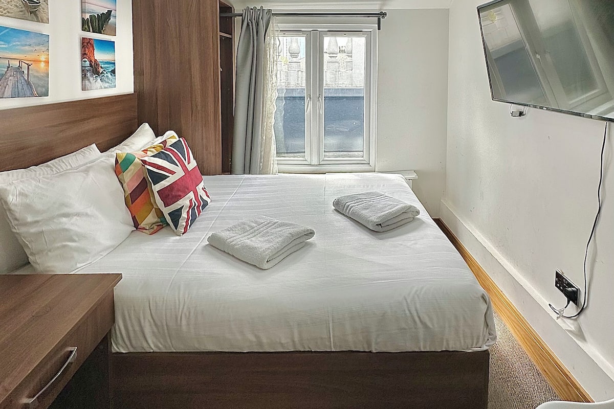 Ein Hotelzimmer mit Bett, Fernseher, Fenster und Bildern an der Wand.