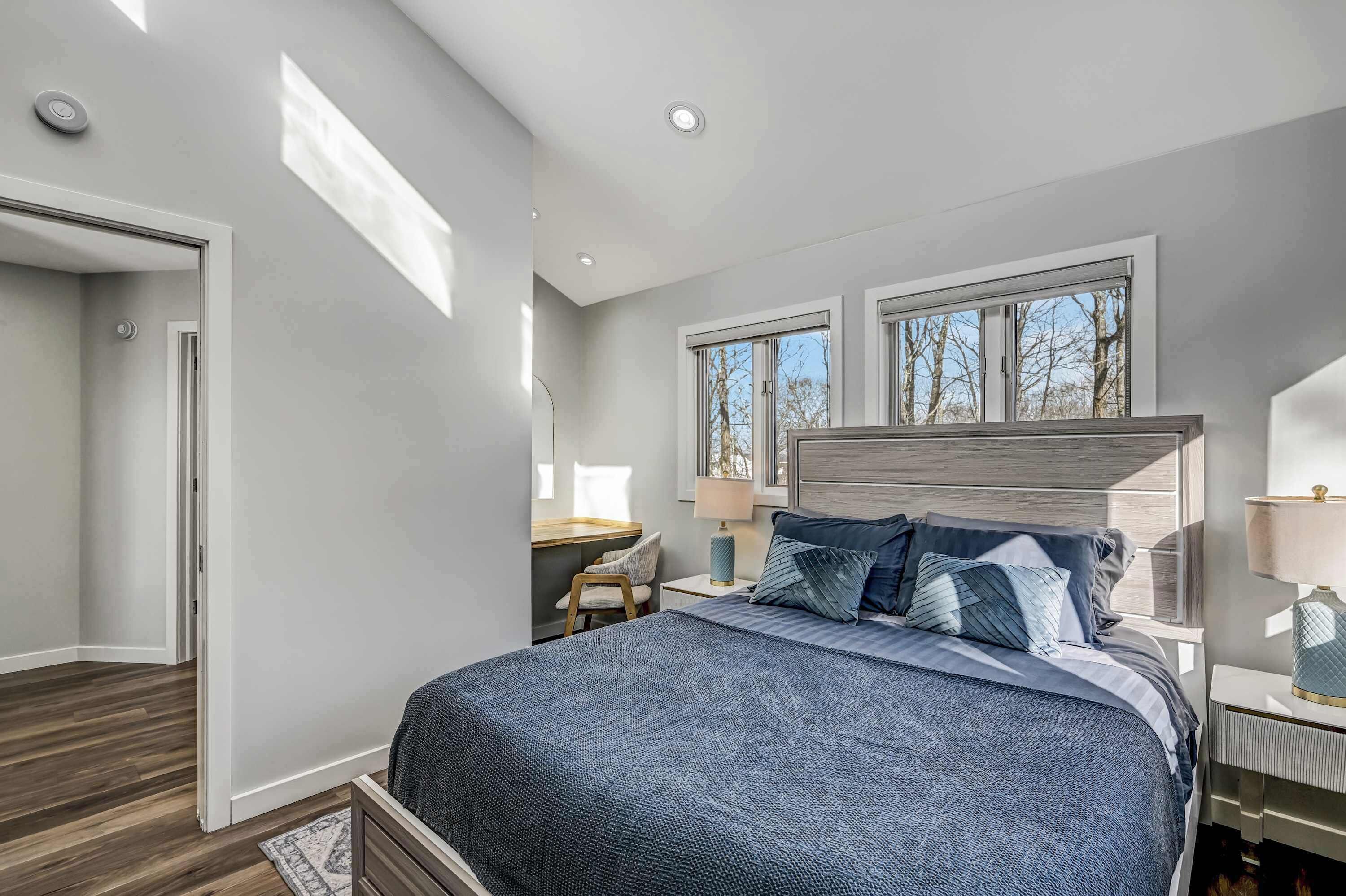 A bedroom with a large bed, a desk, and two windows.