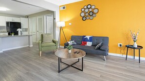 A modern living room with a grey sofa, a green armchair, and a coffee table. There is a kitchen area in the background with white cabinets and a black refrigerator. - Chic 2-bedroom apartment with WiFi, AC in marvelous Austin (Austin)