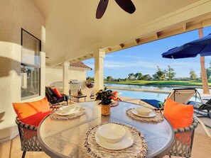 A covered patio with a round table set for dining, outdoor seating, and a view of a golf course and lake. - 4BR w lake view, hot tub, ping pong (Chandler)