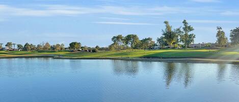 A serene golf course with a calm lake, well-maintained grass, and scattered trees.