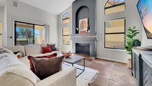 A spacious living room with a fireplace, large windows, and a ceiling fan. - 4BR w lake view, hot tub, ping pong (Chandler)