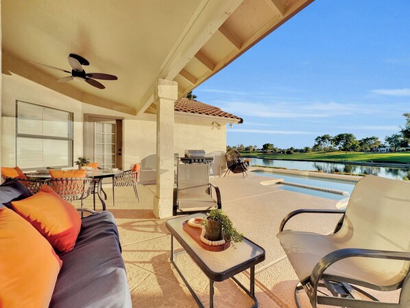 A covered patio with outdoor seating, a grill, and a view of a golf course and lake. - 4BR w lake view, hot tub, ping pong (Chandler)