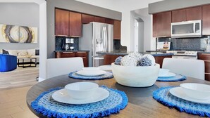 A modern kitchen with dark wooden cabinets, stainless steel appliances, and a dining area with a round table set with white plates and bowls.